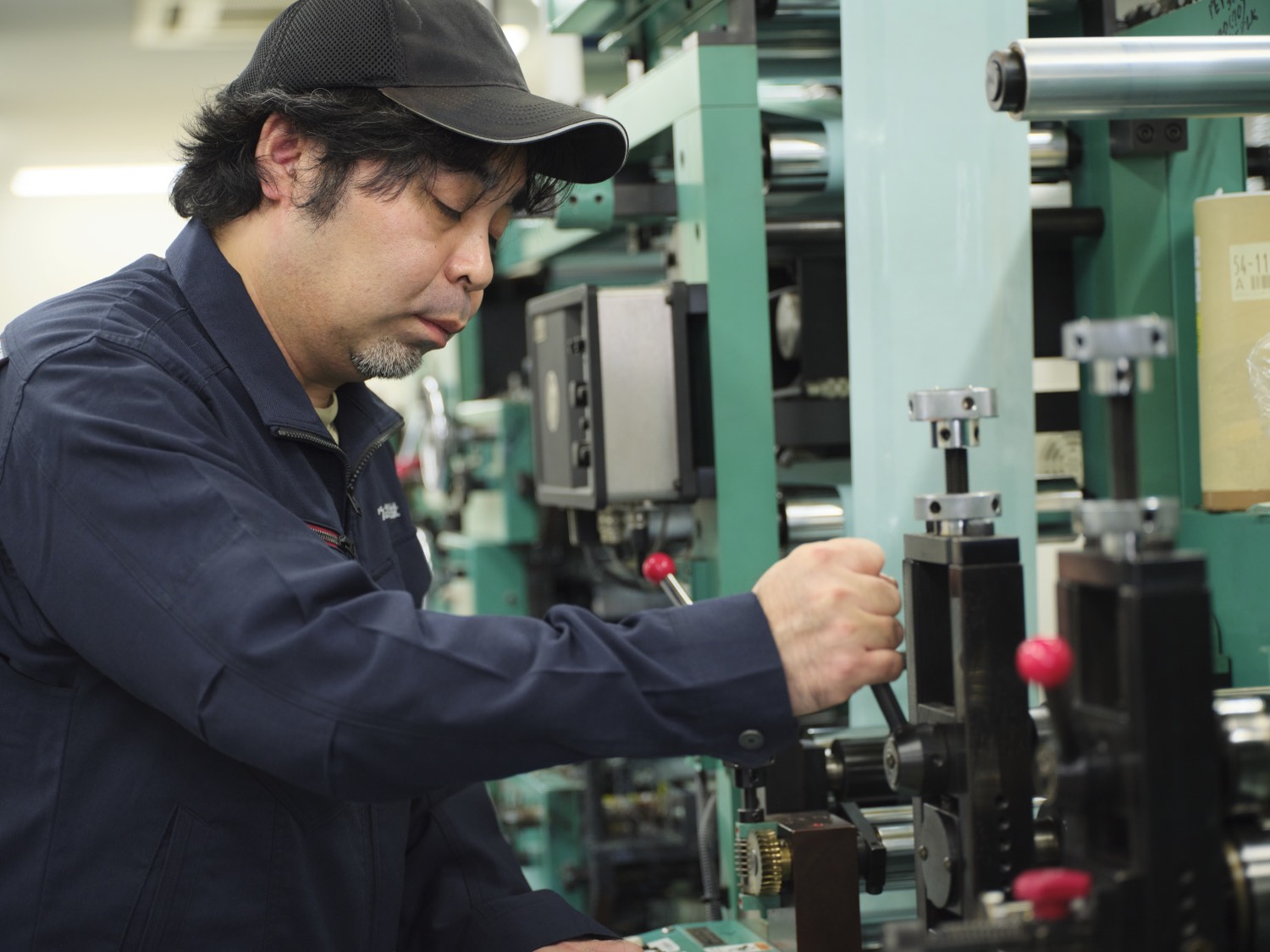 緑の印刷機を工具で調整する熟練オペレーター